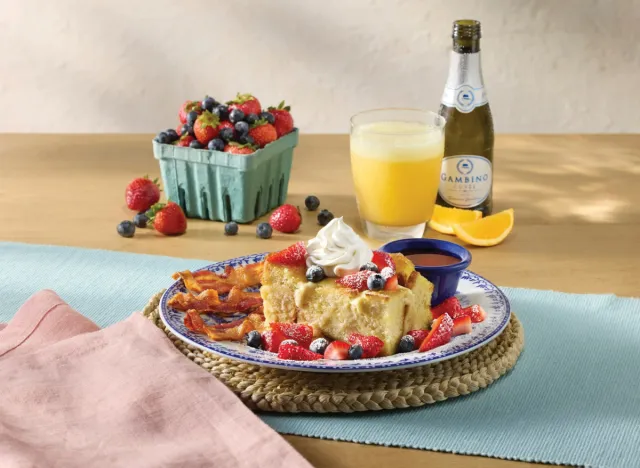 cracker barrel's fresh berry french toast bake with mimosa, champagne, and a container of strawberries and blueberries