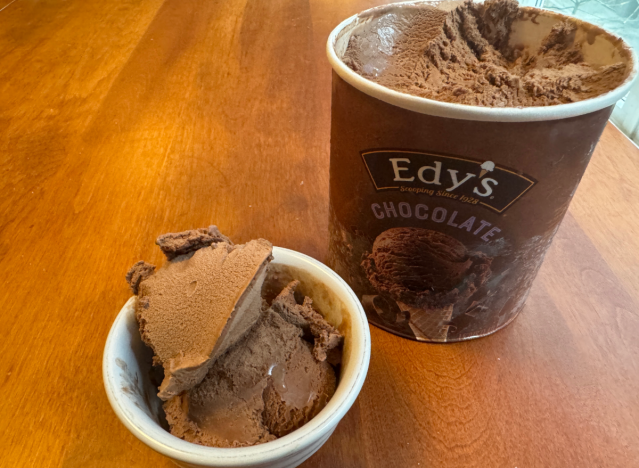 a pint of edy's chocolate ice cream open on a table with a bowl of ice cream.