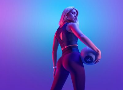 fit woman in fitness attire holding a medicine ball in front of blue and purple backdrop