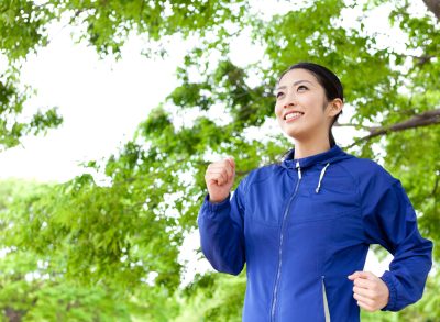 happy woman in blue jacket walking for exercise outdoors under green foliage