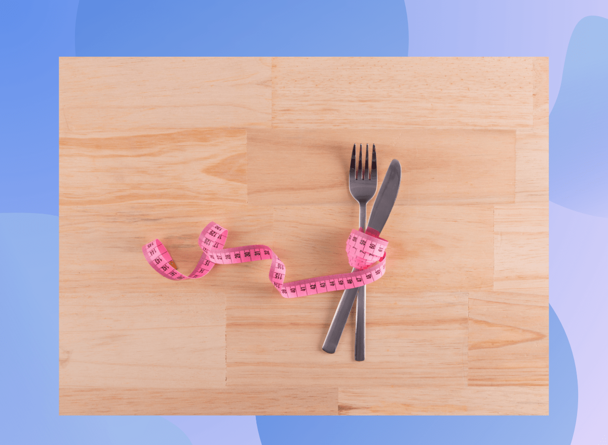 tape measure wrapped around knife and fork on wood floor, concept of weight loss