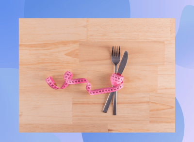 tape measure wrapped around knife and fork on wood floor, concept of weight loss