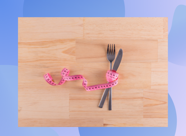 tape measure wrapped around knife and fork on wood floor, concept of weight loss