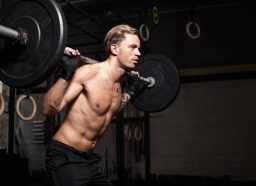 fit, muscular man getting ready to do barbell squats in dark gym