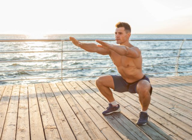 fit man doing squats on boardwalk by the ocean at sunrise or sunset
