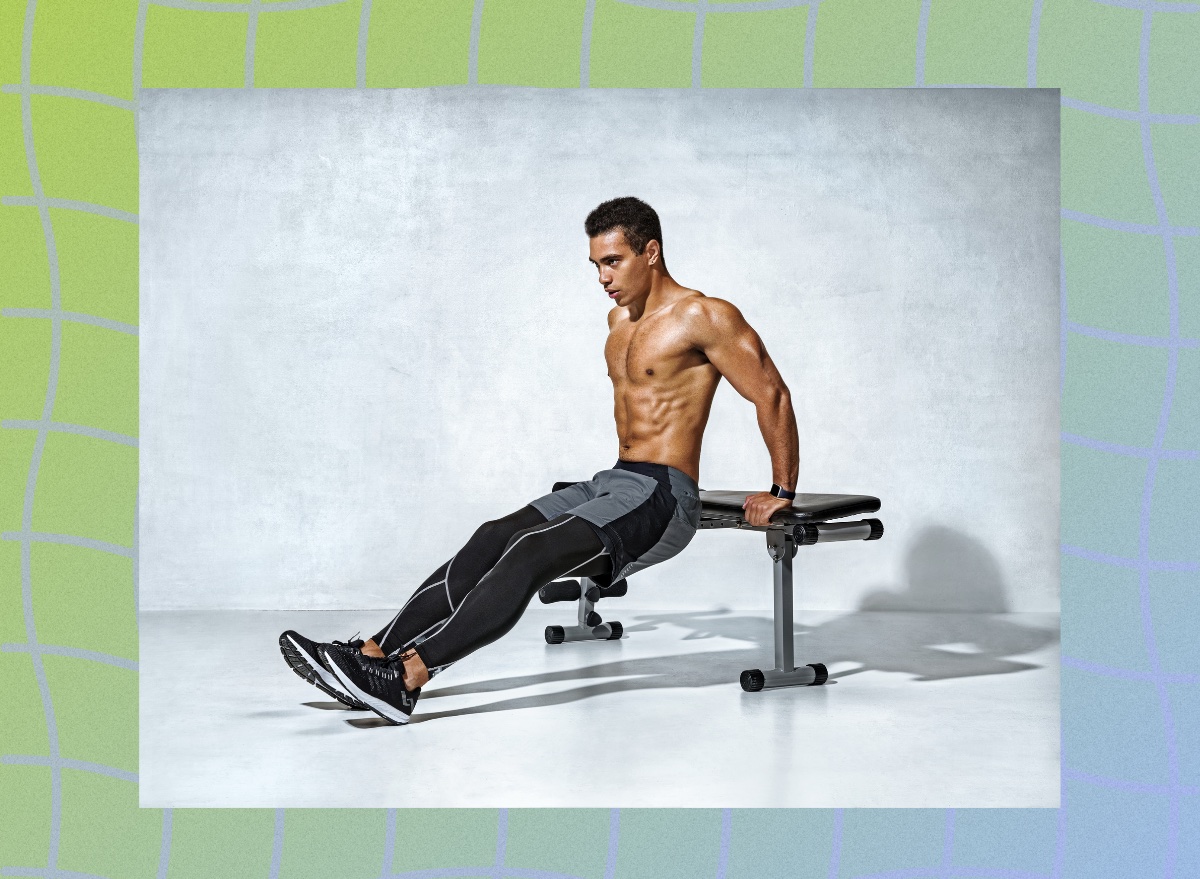 muscular man doing tricep dips from workout bench in front of gray backdrop