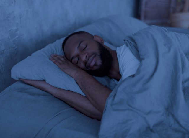 man sleeping peacefully in dark room with gray sheets