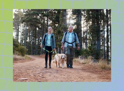 mature happy couple wearing backpacks hiking on a trail with their dog, surrounded by trees