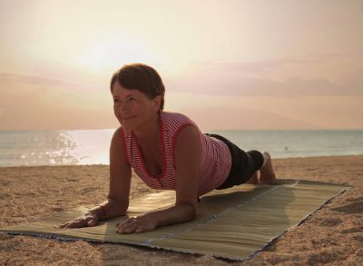 mature woman doing beach yoga plank on straw mat at sunrise or sunset