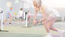 mature woman with gray hair in tennis dress playing tennis in indoor court