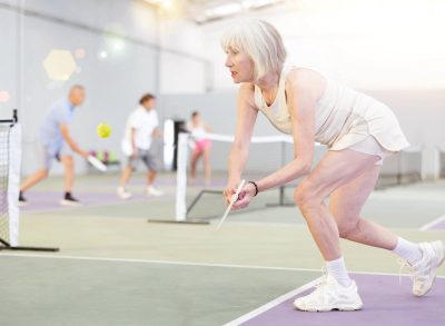 mature woman with gray hair in tennis dress playing tennis in indoor court