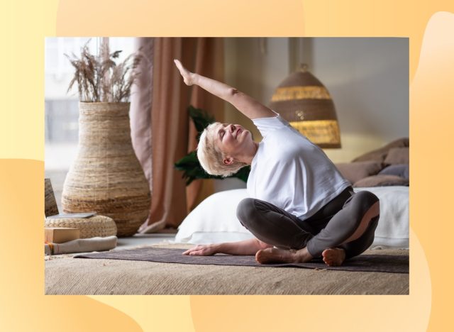 mature woman with short blonde hair stretching in boho bedroom on yoga mat