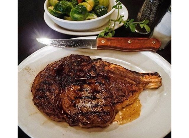morton's bone in ribeye steak on a plate with a side of brussel sprouts.