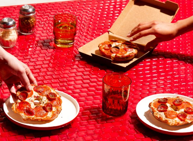 hands reaching for pizza hut's new big new yorker pizza bagels on a red table with red drinking glasses
