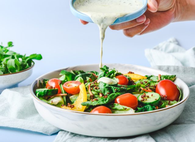 hand pouring bowl of salad dressing on top of salad