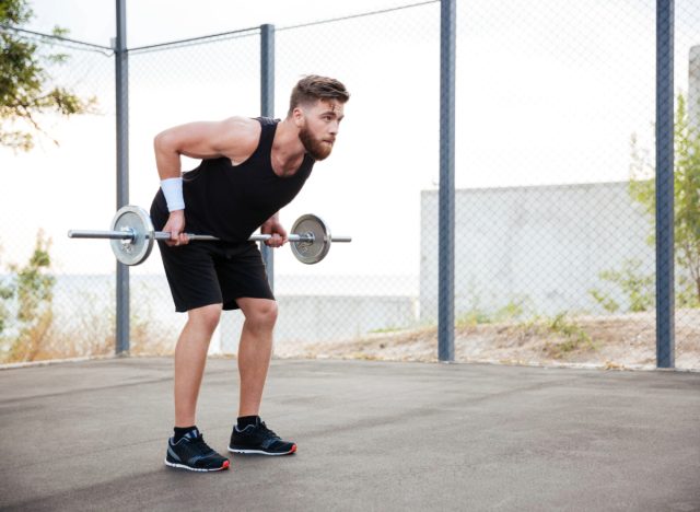 fit, focused man doing reverse grip barbell rows outdoors on cement court