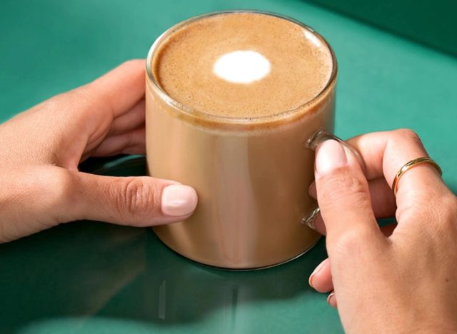 hands holding a mug of starbucks flat white on a green background.