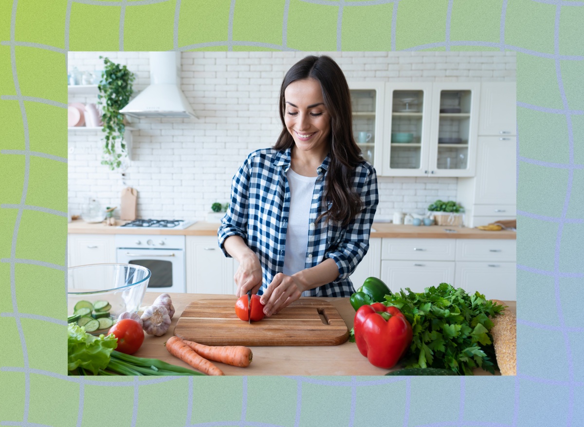brunette woman wearing plaid shirt cutting tomato on cutting board in bright white kitchen