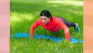 fit, focused woman in red zip-up and workout leggings doing pushups on blue yoga mat in the grass on sunny day