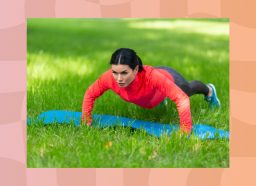 fit, focused woman in red zip-up and workout leggings doing pushups on blue yoga mat in the grass on sunny day