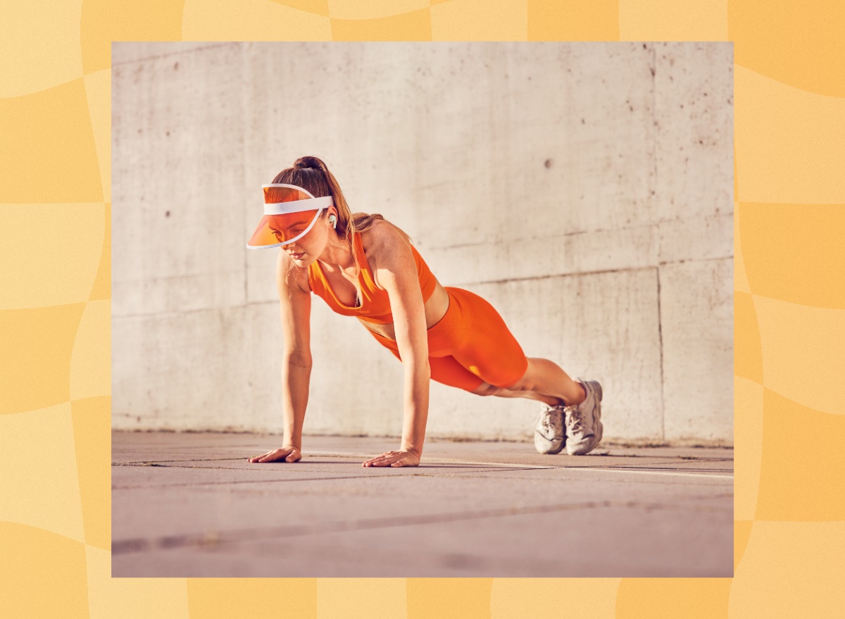 fit woman in orange workout attire and orange visor doing pushups outdoors on cement