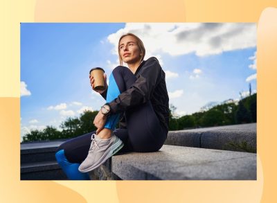 woman in athletic attire sitting outside and holding to-go coffee cup after workout