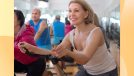 mature blonde woman with short hair wearing white tank top on indoor cycling bike in exercise class at the gym