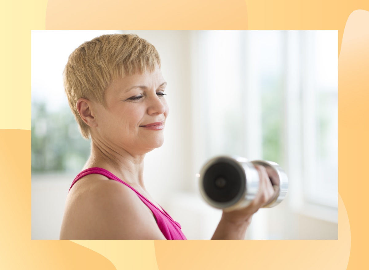 close-up of mature woman with short blonde hair wearing a pink activewear tank top lifting dumbbell in her bright home