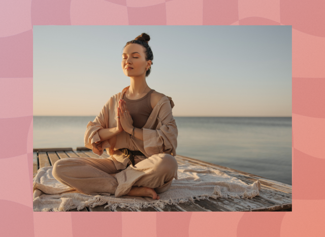 peaceful brunette woman in breezy yoga apparel meditating on boho blanket on dock by ocean at sunrise