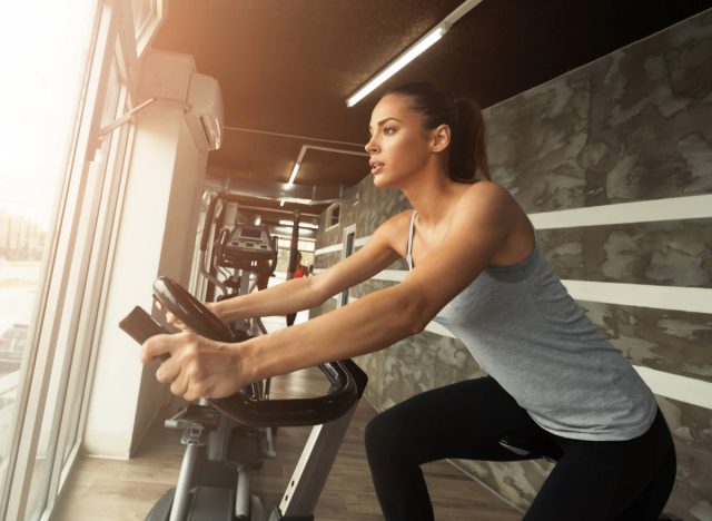 fit woman riding on a stationary bike at the gym, looking out a window