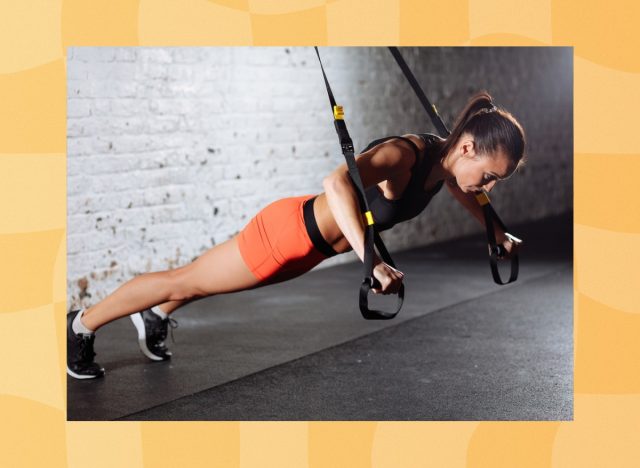 fit brunette woman wearing orange biker shorts and black sports bra doing TRX exercise at the gym