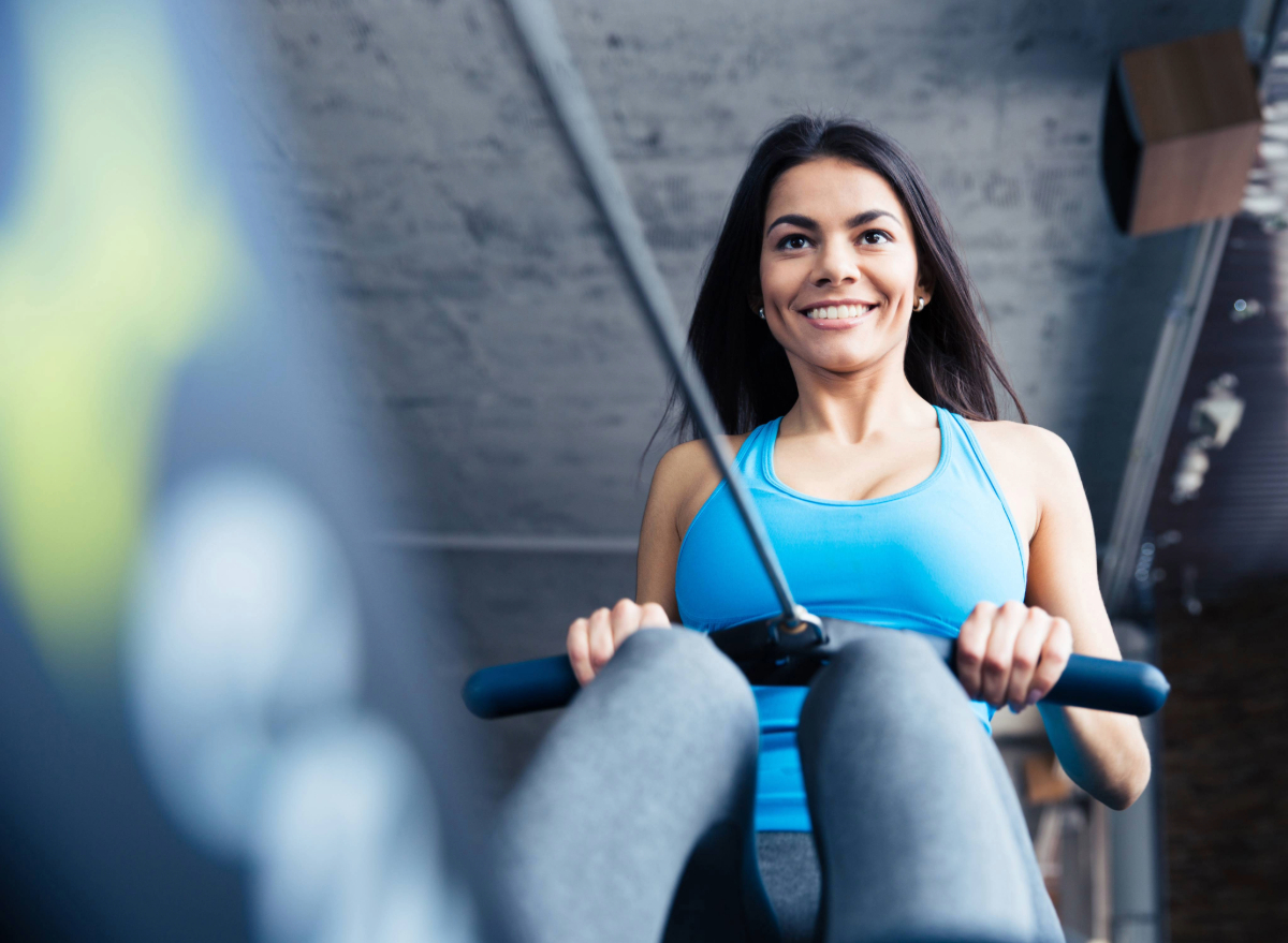 fit, happy brunette woman using rowing machine at the gym