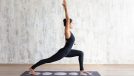 fit woman in black onesie doing yoga pose in bright room on top of moon-themed yoga mat