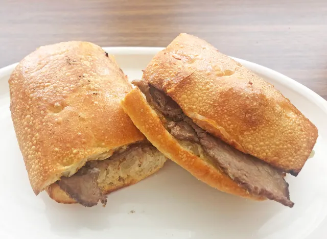 a panera cheesesteak sandwich cut in half on a white plate.