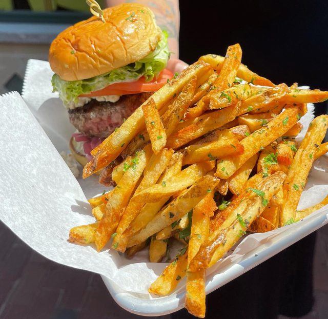 A pile of golden french fries on a platter next to a burger from DNB Craft Kitchen