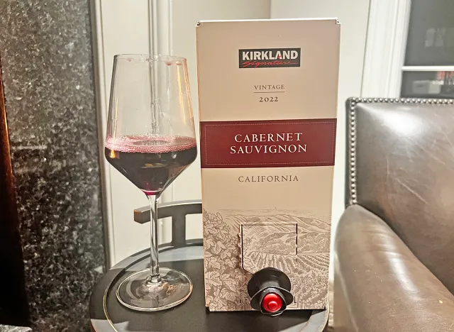 A box and glass of Costco's Kirkland Signature cabernet sauvignon on table.