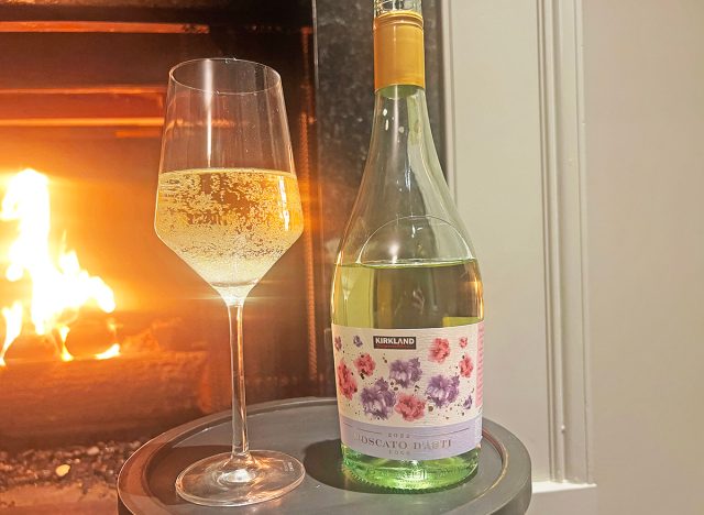 Costco's Kirkland Signature moscato glass and bottle by fireplace.