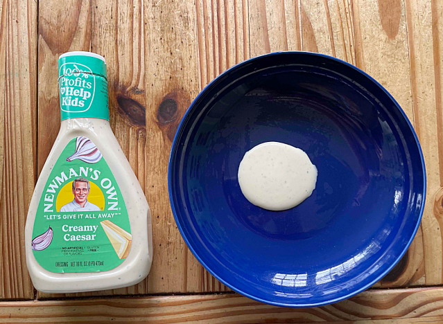 a bottle of caesar dressing next to a blue plate with dressing on it.