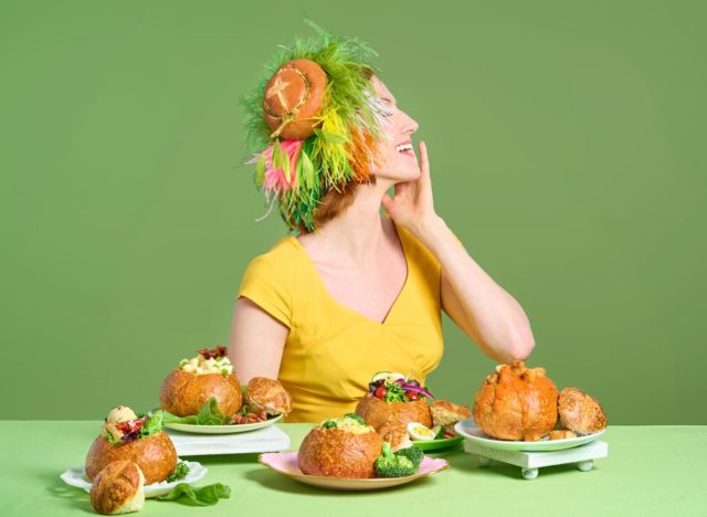 Woman wearing a Panera Bread Head hat next to table with several Panera bread bowls