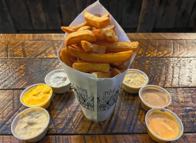 A conical shaped container of french fries surrounded by various dipping sauces at Pommes Frites NYC
