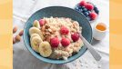 bowl of oatmeal with raspberries, slice banana, and almonds next to smaller bowl of berries and a little server of honey