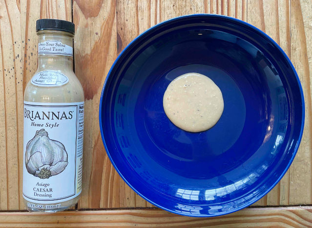 a bottle of caesar dressing next to a blue plate with dressing on it.