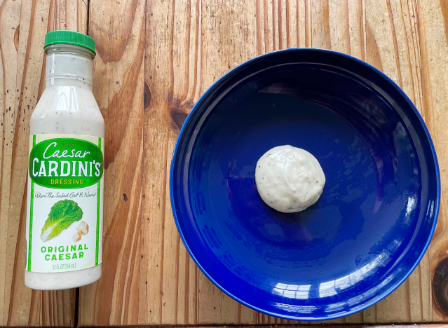 a bottle of caesar dressing next to a blue plate with dressing on it.