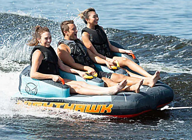 3 people on an inflatable raft being towed by a boat.