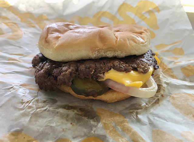 a burger with cheese and pickles on paper. 