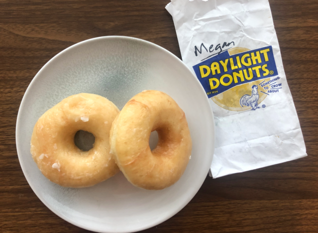 two glazed donuts on a plate with a daylight donuts bag.
