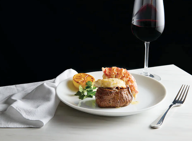 a filet mignon and a lobster tail with a glass of wine