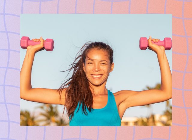 fit, happy brunette woman doing dumbbell shoulder press with pink dumbbells outdoors around sunset
