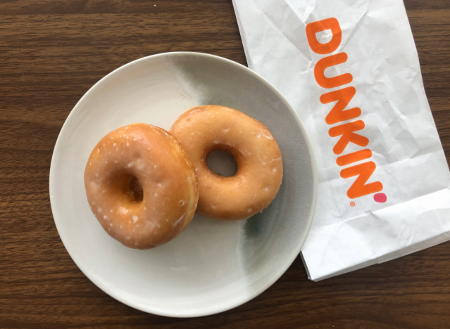 two glazed donuts ona plate with a dunkin bag.
