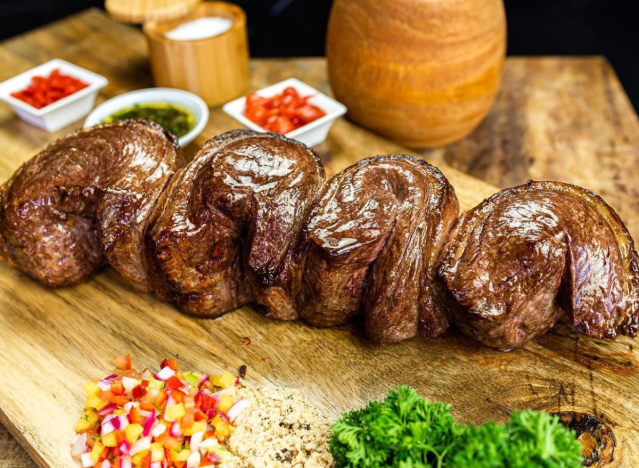 a row of steaks on a cutting board with garnishes.